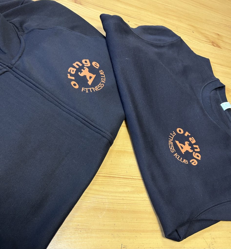 Dwie czarne bluzy z pomarańczowym logo Orange Fitness Klub na lewej piersi, JustWearIt.pl, Środa Wielkopolska